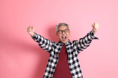 40 'lı yaşlarda Asyalı bir adam pembe arka planda sıradan kıyafetlerle dolanıyor..