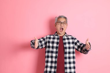 40 'lı yaşlarda Asyalı bir adam pembe arka planda sıradan kıyafetlerle dolanıyor..