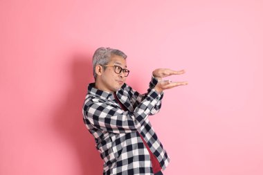 40 'lı yaşlarda Asyalı bir adam pembe arka planda sıradan kıyafetlerle dolanıyor..