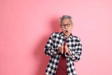 40 'lı yaşlarda Asyalı bir adam pembe arka planda sıradan kıyafetlerle dolanıyor..