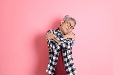 40 'lı yaşlarda Asyalı bir adam pembe arka planda sıradan kıyafetlerle dolanıyor..