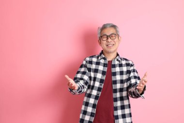 40 'lı yaşlarda Asyalı bir adam pembe arka planda sıradan kıyafetlerle dolanıyor..