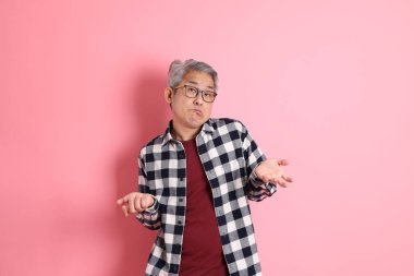 40 'lı yaşlarda Asyalı bir adam pembe arka planda sıradan kıyafetlerle dolanıyor..