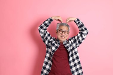 40 'lı yaşlarda Asyalı bir adam pembe arka planda sıradan kıyafetlerle dolanıyor..