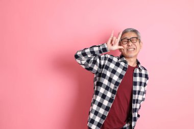 40 'lı yaşlarda Asyalı bir adam pembe arka planda sıradan kıyafetlerle dolanıyor..