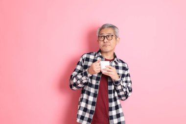 40 'lı yaşlarda Asyalı bir adam pembe arka planda sıradan kıyafetlerle dolanıyor..