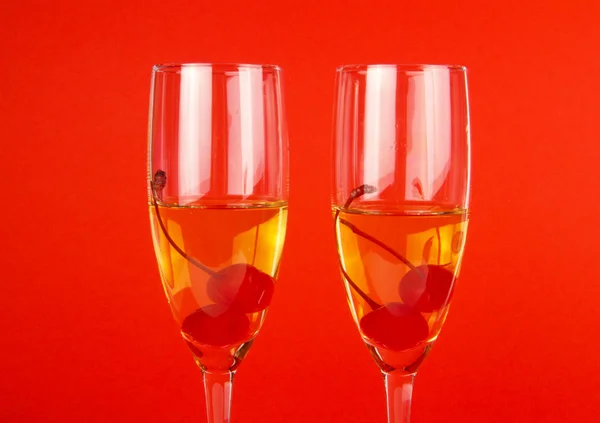 Twee champagneglazen met kersen op rood — Stockfoto