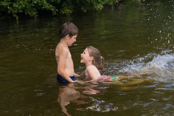 Маленький мальчик учит свою младшую сестру плавать в озере — стоковое фото