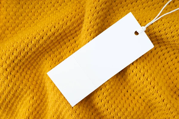 Etiqueta blanca de ropa rectangular en blanco sobre fondo de tela de punto amarillo —  Fotos de Stock