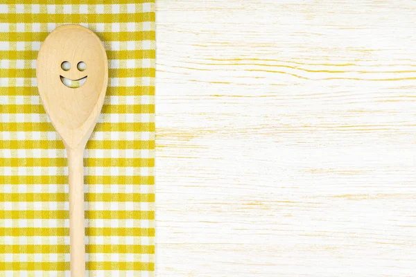 Tahta kaşık, beyaz tahta yüzeyde sarı kareli masa örtüsünde gülümseme. Menü, yemek tarifi, restoran ve web sitesi için maket. Mutfak yemek arka planı, şablon, kopyalama alanı olan düz uzanma