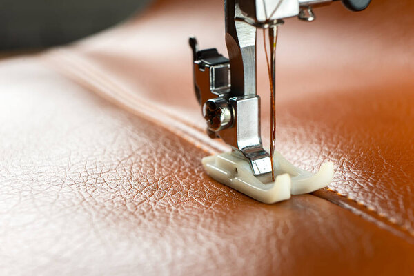 Современная швейная машинка прижимной лапкой с иглой шьет коричневую кожу. Процесс шитья декоративного шва на коже специальной кожаной пресс-стопой. Закрыть, скопировать.