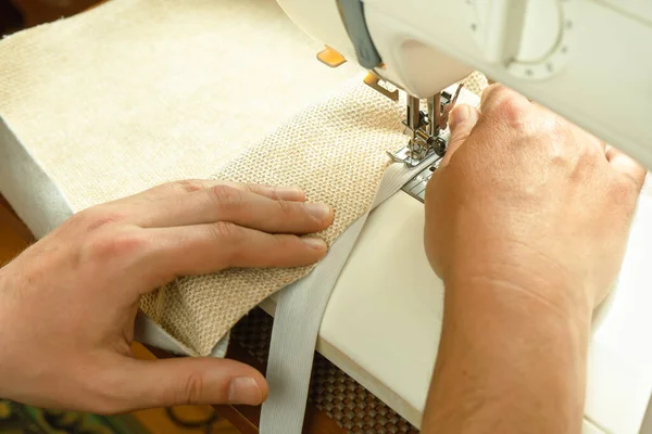 Seamstress hands holding white textile fabric. Male hands stitching white fabric on modern sewing machine at workplace. Close up view of sewing process. Handmade, hobby, small business concept
