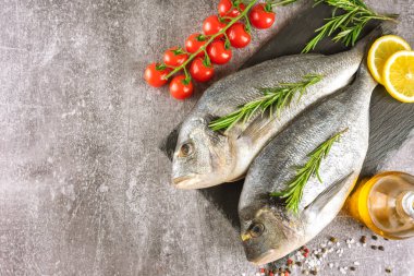 Taze balık dorado ve pişirmek için malzemeler. Çiğ balık dorada baharatlar ve bitkiler gri beton masa üzerinde. Deniz ürünleri, restoran, diyet, sağlıklı yemek geçmişi. Üst görünüm, kopyalama alanı olan düz uzanma