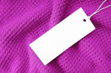 White blank rectangular clothing tag, label mockup template on purple knitted fabric background . Price tag label with copy space for text. Shopping, sale, price, fashion, discount concept