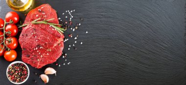 Raw beef steak with spices and ingredients for cooking on black slate background. Banner for restaurant menu, header for web sites. Top view, flat lay, mockup with copy space for text