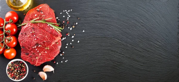Raw beef steak with spices and ingredients for cooking on black slate background. Banner for restaurant menu, header for web sites. Top view, flat lay, mockup with copy space for text