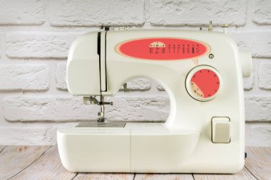 Modern multi operation sewing machine, assortment of different stitches for decorating clothes on table in tailor's workshop or atelier on white brick background.