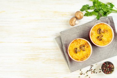 Chicken and mushroom casserole with golden crust, julienne with baked cheese, creamy gratin in portion ramekin clay pot on white wooden background. French cuisine. Top view, flat lay with copy space
