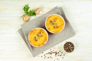 Chicken and mushroom casserole with golden crust, julienne with baked cheese, creamy gratin in portion ramekin clay pot on white wooden background. French cuisine. Top view, flat lay