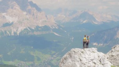 Belluno, Ağustos 2020. İki genç arkadaş bir kayanın üstündeki ufka hayran. Sırt çantaları ve spor giysileriyle donatılmışlardır çünkü güneşli bir yaz gününde dolomitler zincirini keşfederler.