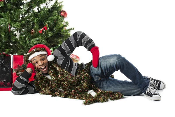 Glücklicher afrikanisch-amerikanischer Mann liegt neben einem Weihnachtsbaum — Stockfoto