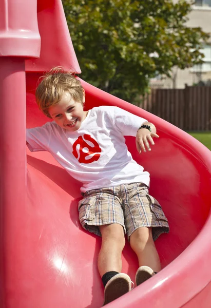 Menino feliz deslizando no slide vermelho — Fotografia de Stock