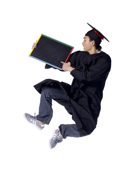 Graduating student jumping while holding black board — Stock Photo, Image