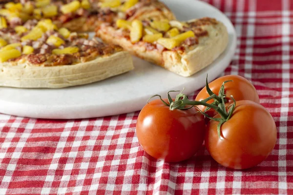 Hawaiian pizza and a whole ripe tomato — Stock Photo, Image