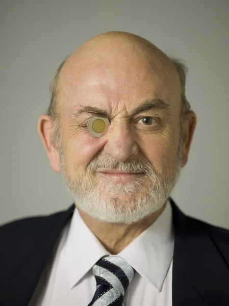 Old businessman with coin on his one eye — Stock Photo, Image