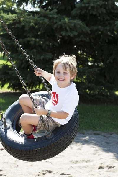 Élémentaire garçon balançant sur pneu swing — Photo