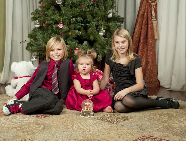 Portrait of brother and sisters sitting on floor with christmas — Stock Photo, Image