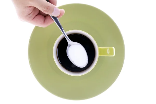 Mano umana tenendo cucchiaio di zucchero sopra tazza e piattino — Foto Stock