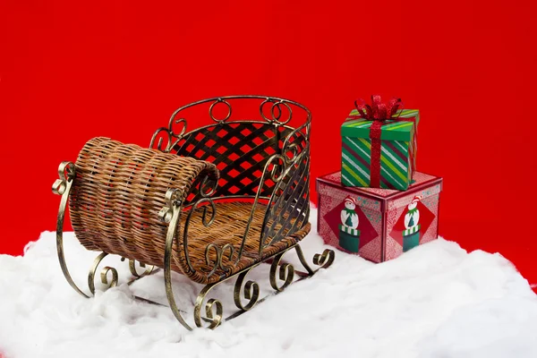 Подарки на снегу рядом с плетеными санями — стоковое фото