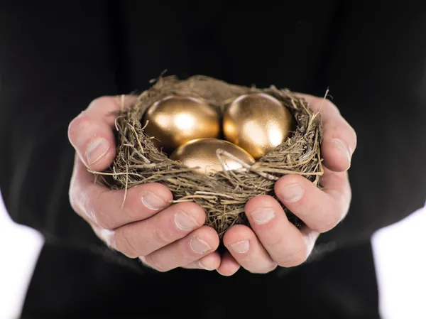 Businessman holding nest with gold eggs — Stock Photo, Image