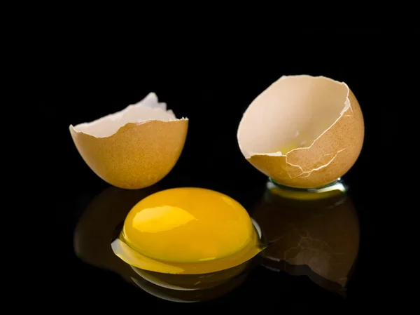 Broken egg with yolk on black surface — Stock Photo, Image