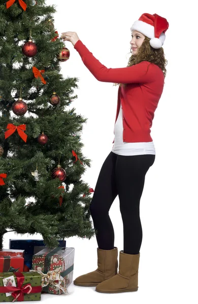 Schöne junge Frau mit Weihnachtsmütze schmückt Weihnachtsbaum — Stockfoto