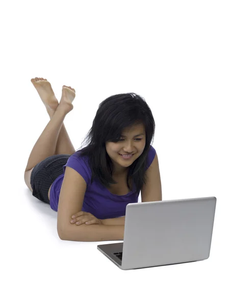 Sonriente mujer joven acostada en el suelo y utilizando el ordenador portátil — Foto de Stock