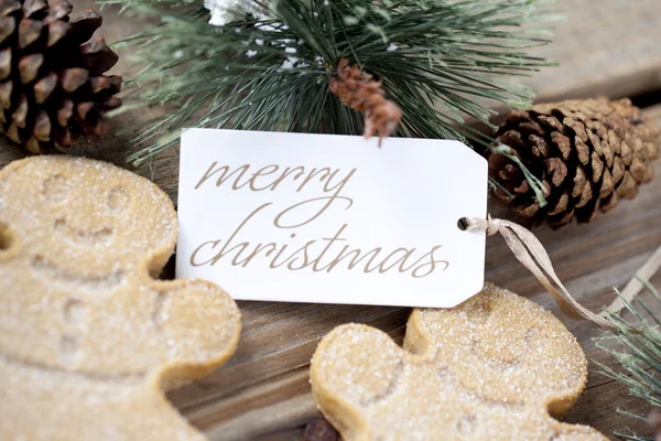 Un allegro cartellino natalizio tra uomini di pan di zenzero e pigne — Foto Stock