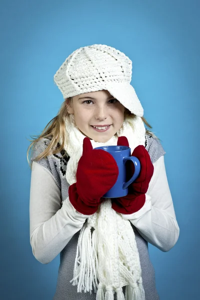 一个年轻的女孩，在一个蓝色的背景上喝热巧克力 — 图库照片