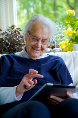 Mutlu yaşlı kadın tablet kullanıyor ve gülüyor.