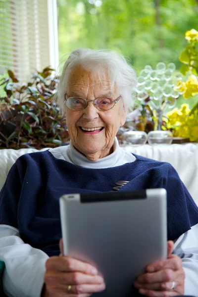 Happy Elderly woman using a tablet looking at the camera and laughing — Stock Photo, Image