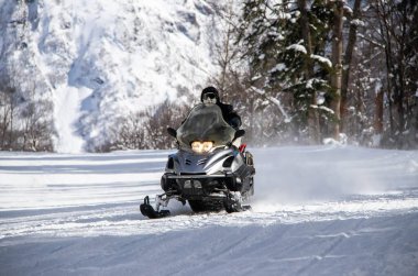 Dağlardaki karlı bir yolda siyah kar motosikletleri sürüyor.