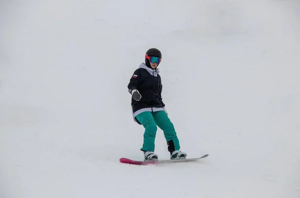 A girl on a snowboard rides down the side of the mountain —  Fotos de Stock