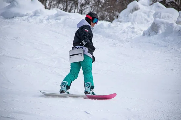 A girl on a snowboard rides down the side of the mountain — 스톡 사진