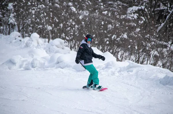 A girl on a snowboard rides down the side of the mountain — 스톡 사진