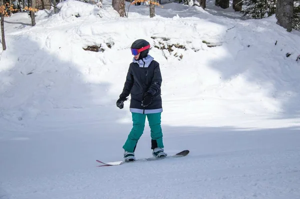 A girl on a snowboard rides down the side of the mountain — 스톡 사진