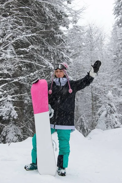 Dziewczyna z snowboardem w lesie w górach i opadami śniegu — Zdjęcie stockowe