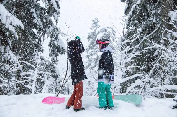 Duas meninas com um snowboards na floresta nas montanhas e a queda de neve — Fotografia de Stock