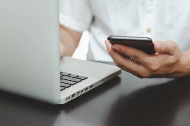 Evdeki masada akıllı telefon ve dizüstü bilgisayar kullanan bir adam internetten bilgi arıyor, evden çalışıyor. İnternet üzerinden iş alışverişi kavramı.