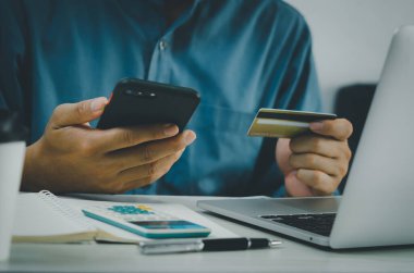 Adamın elinde kredi kartı ve cep telefonu çevrimiçi alışveriş e-ticaret ve masa başında internet bankacılığı var..